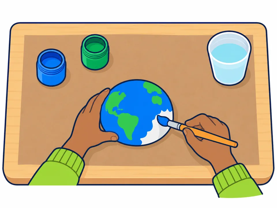 Una mano sostiene la media bola de unicel por los bordes, con la cara plana hacia abajo, y la otra pinta de azul la parte curva; ya tiene algunos continentes verdes, y en la mesa hay botes de pintura azul y verde y un vaso de agua.